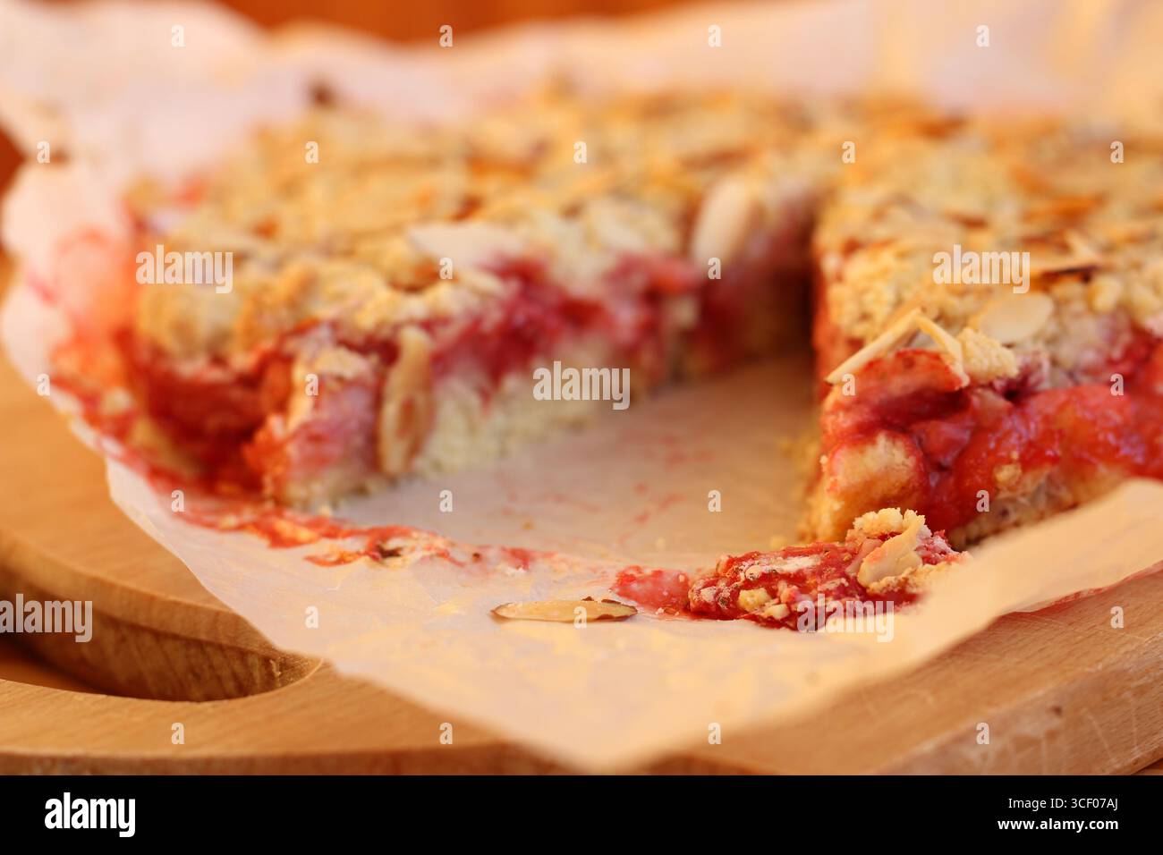 Tarte au crumble aux fraises et aux amandes fraîchement cuite avec garniture croquante sur papier parchemin. Remplissage de baies juteuses, croûte dorée, style rustique, fond flou Banque D'Images