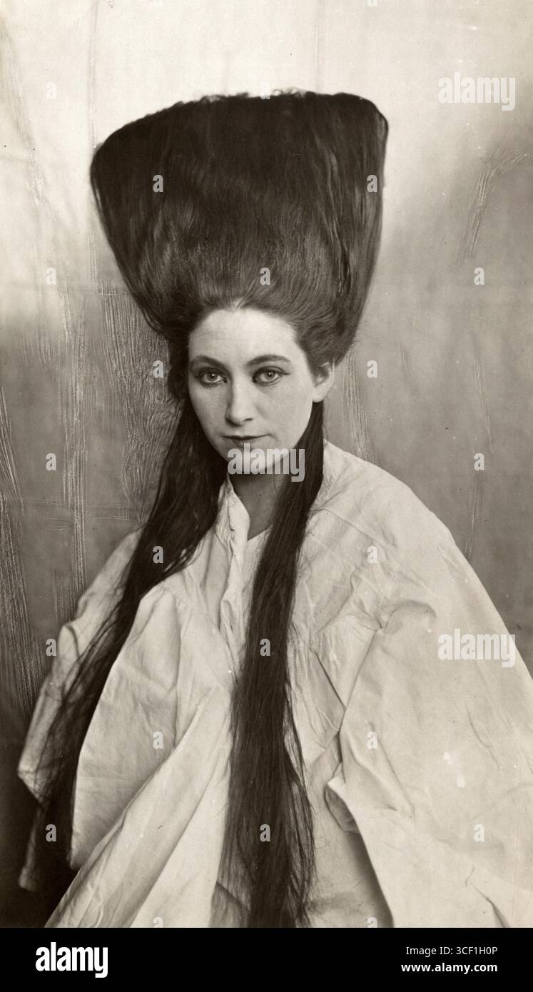 Une femme aux cheveux longs, assise dans un fauteuil de coiffeur, obtenant une coiffure Louis XVI semblable à la mode de Marie-Antoinette, pays-Bas, 1922. Banque D'Images