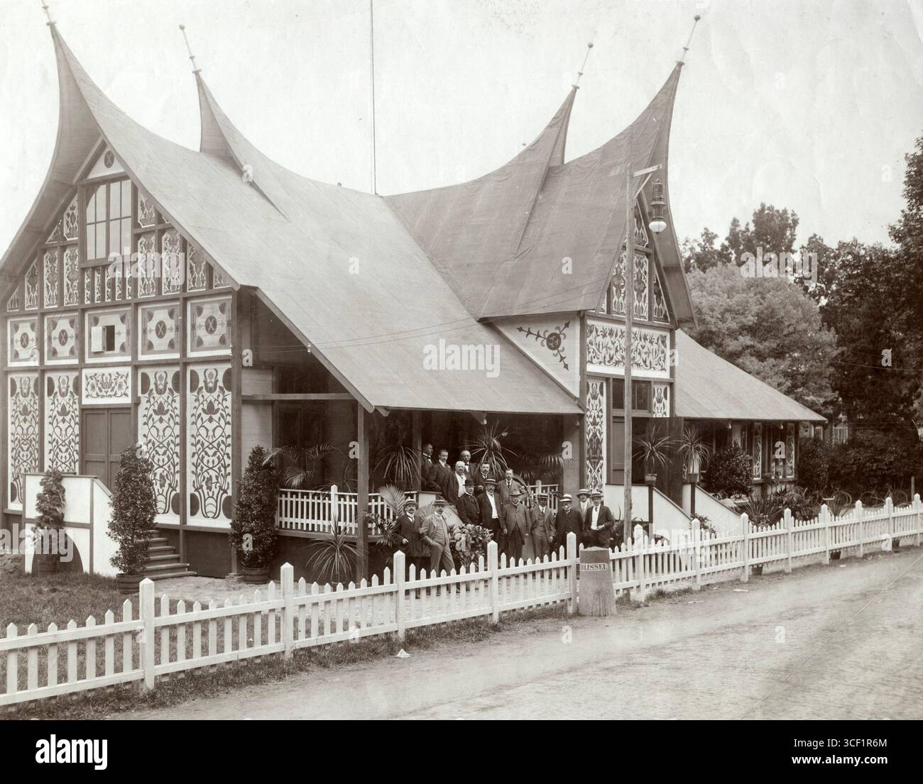 Lors de l'exposition coloniale agricole de Deventer, aux pays-Bas, en 1912, un bâtiment conçu dans le style indonésien présentait des murs magnifiquement peints. Les visiteurs, certains portant des chapeaux de paille, se tenaient sur la véranda et dans le jardin. Banque D'Images