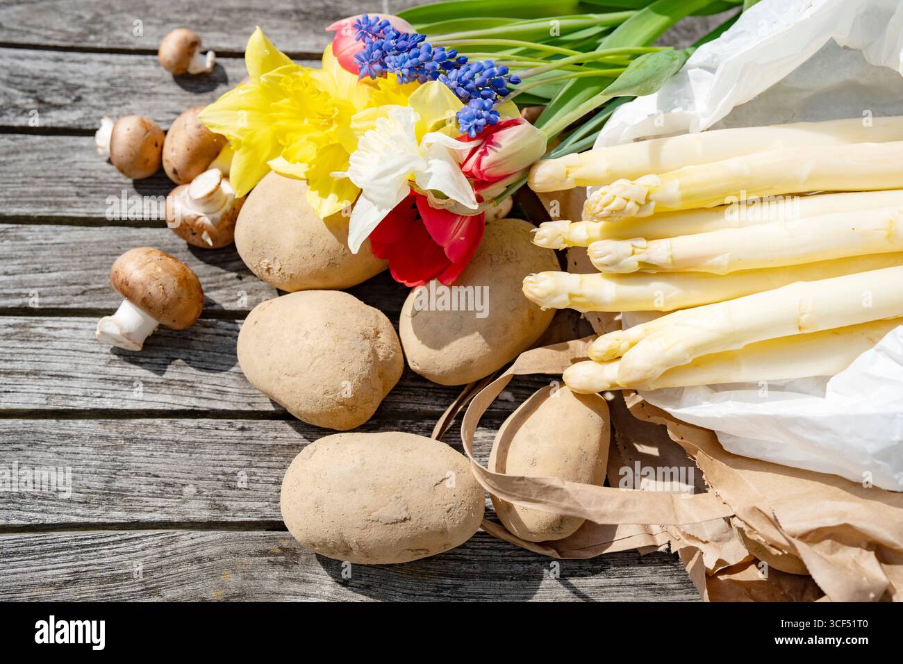 Asperges blanches et fleurs colorées sur bois gris. Légumes frais et diverses fleurs de saison. Banque D'Images