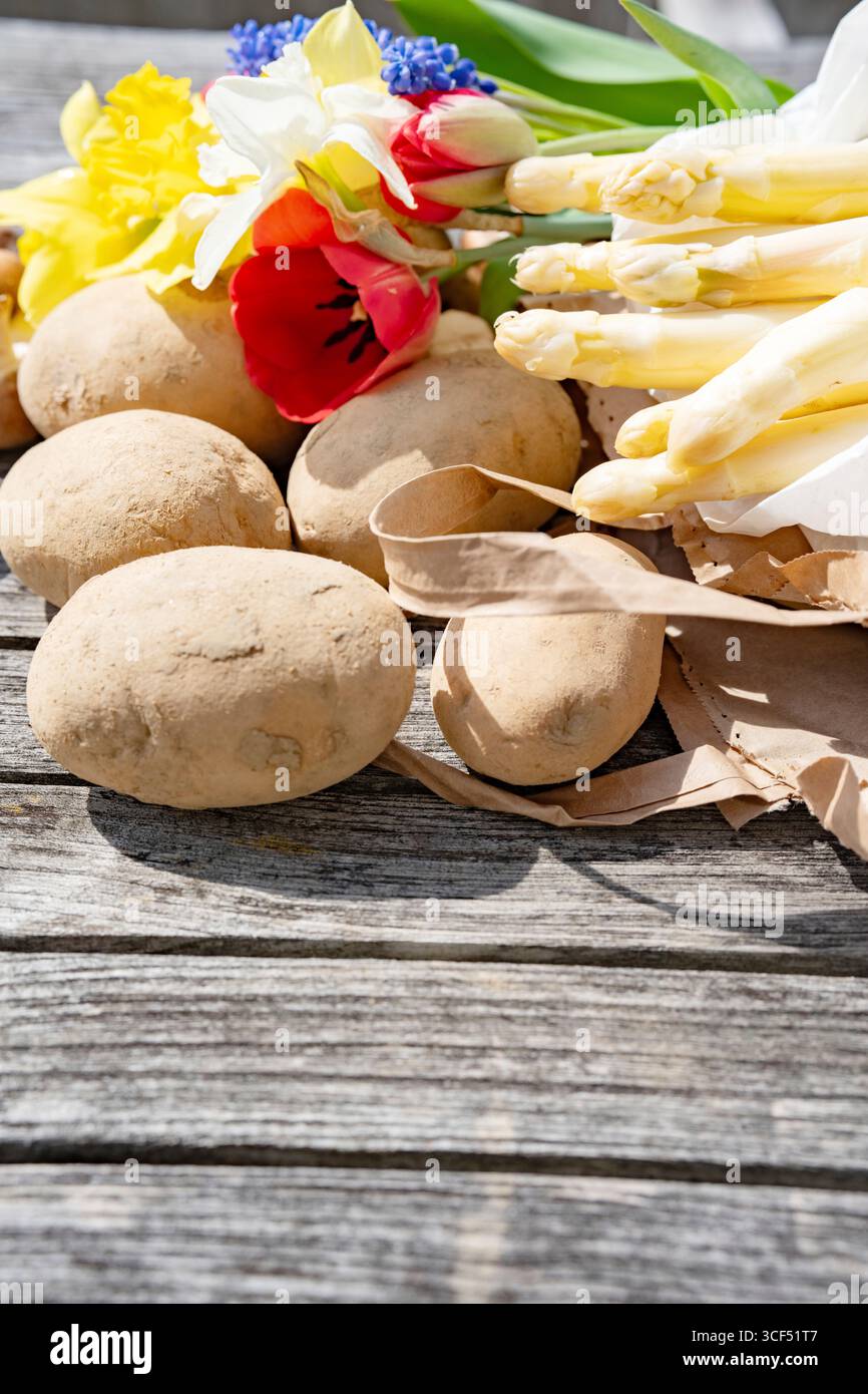Asperges blanches et fleurs colorées sur bois gris. Légumes frais et diverses fleurs de saison. Banque D'Images