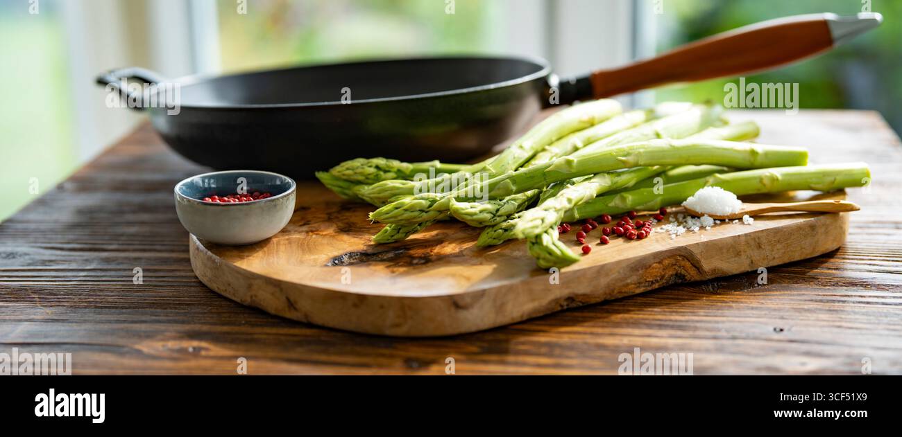 Ingrédients pour rôtir les asperges vertes. Légumes locaux et une poêle en fonte avec poignée en bois sur bois rustique. Préparation de légumes frais pour une alimentation saine. Banque D'Images