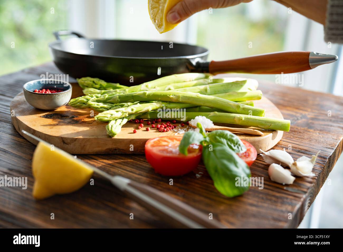 Ingrédients frais pour asperges vertes rôties. Légumes locaux et une poêle en fonte sur une table en bois rustique. Gouttes de citron pour la fraîcheur. Gros plan avec faible profondeur de champ. Banque D'Images