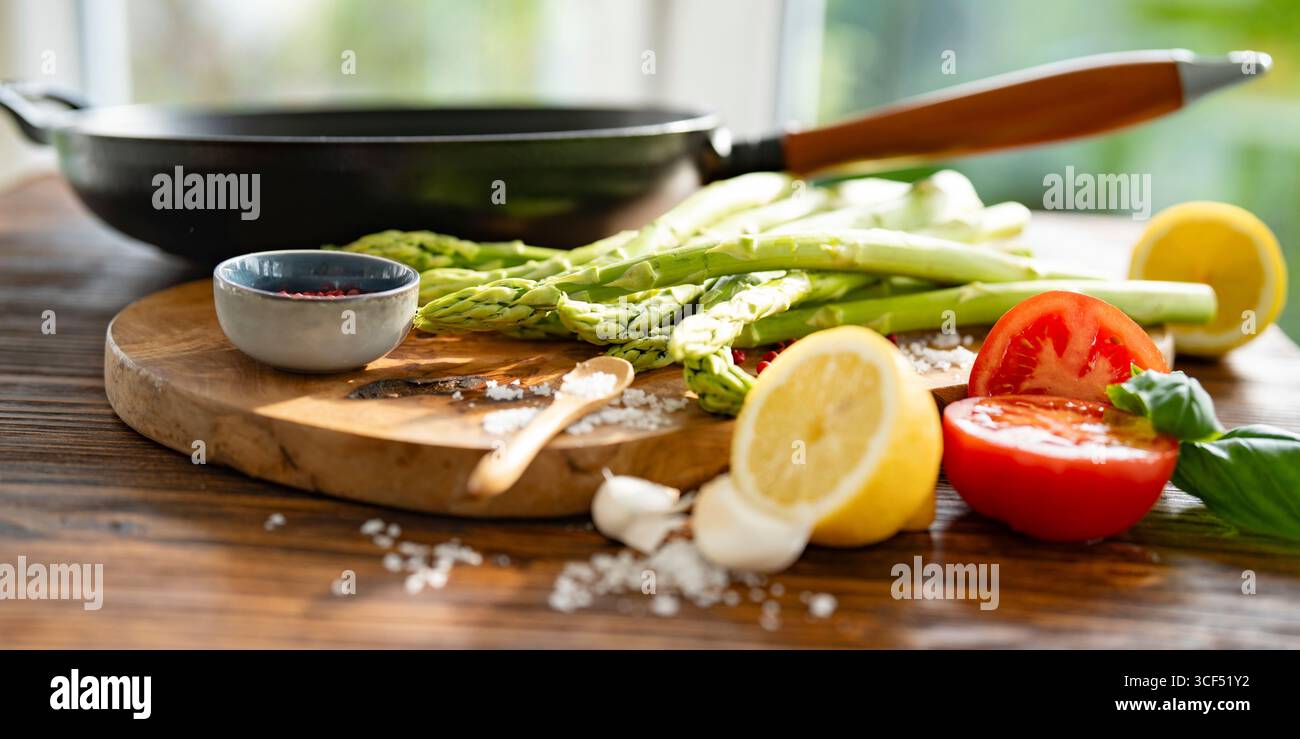 Ingrédients pour rôtir les asperges vertes. Légumes locaux et une poêle en fonte avec poignée en bois sur bois rustique. Préparation de légumes frais pour une alimentation saine. Banque D'Images
