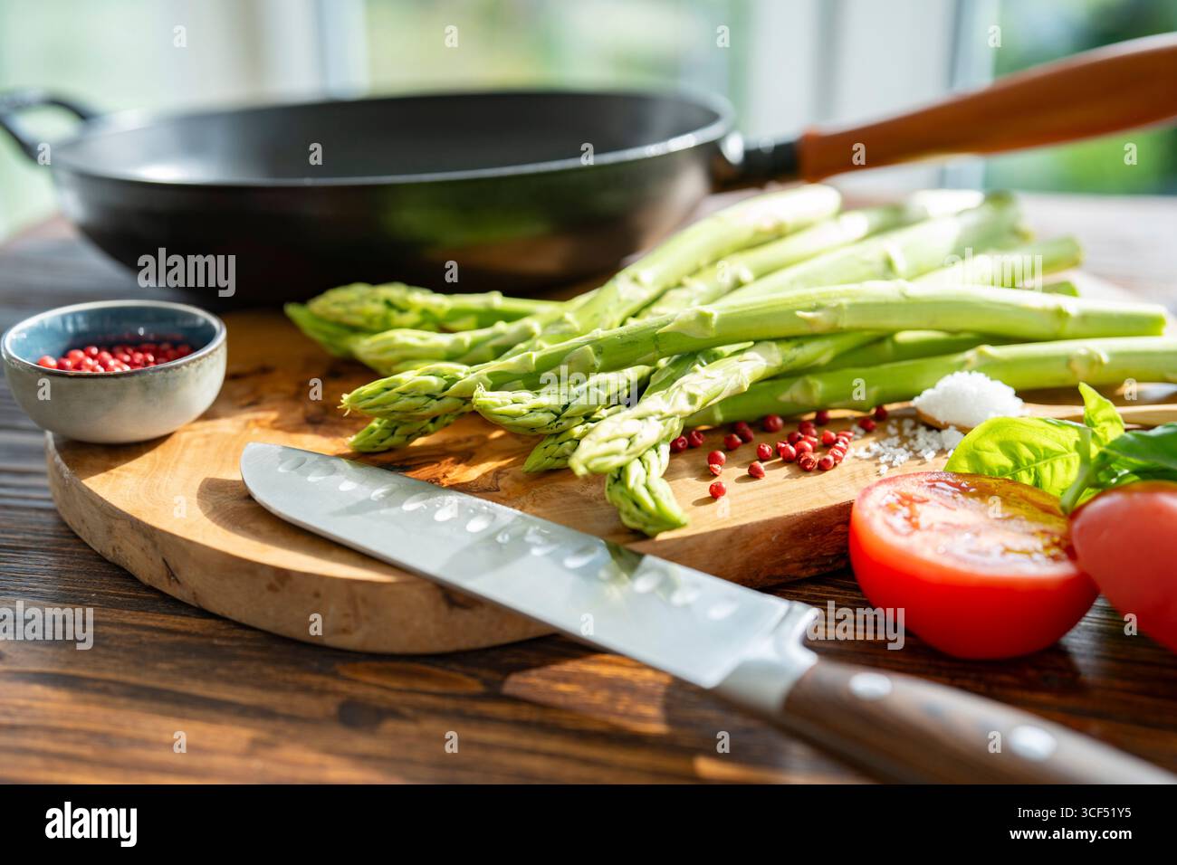 Asperges vertes et ingrédients à rôtir dans une poêle. Légumes frais locaux et une poêle en fonte sur une planche à découper en bois. Préparer et cuisiner pour une alimentation saine. Banque D'Images