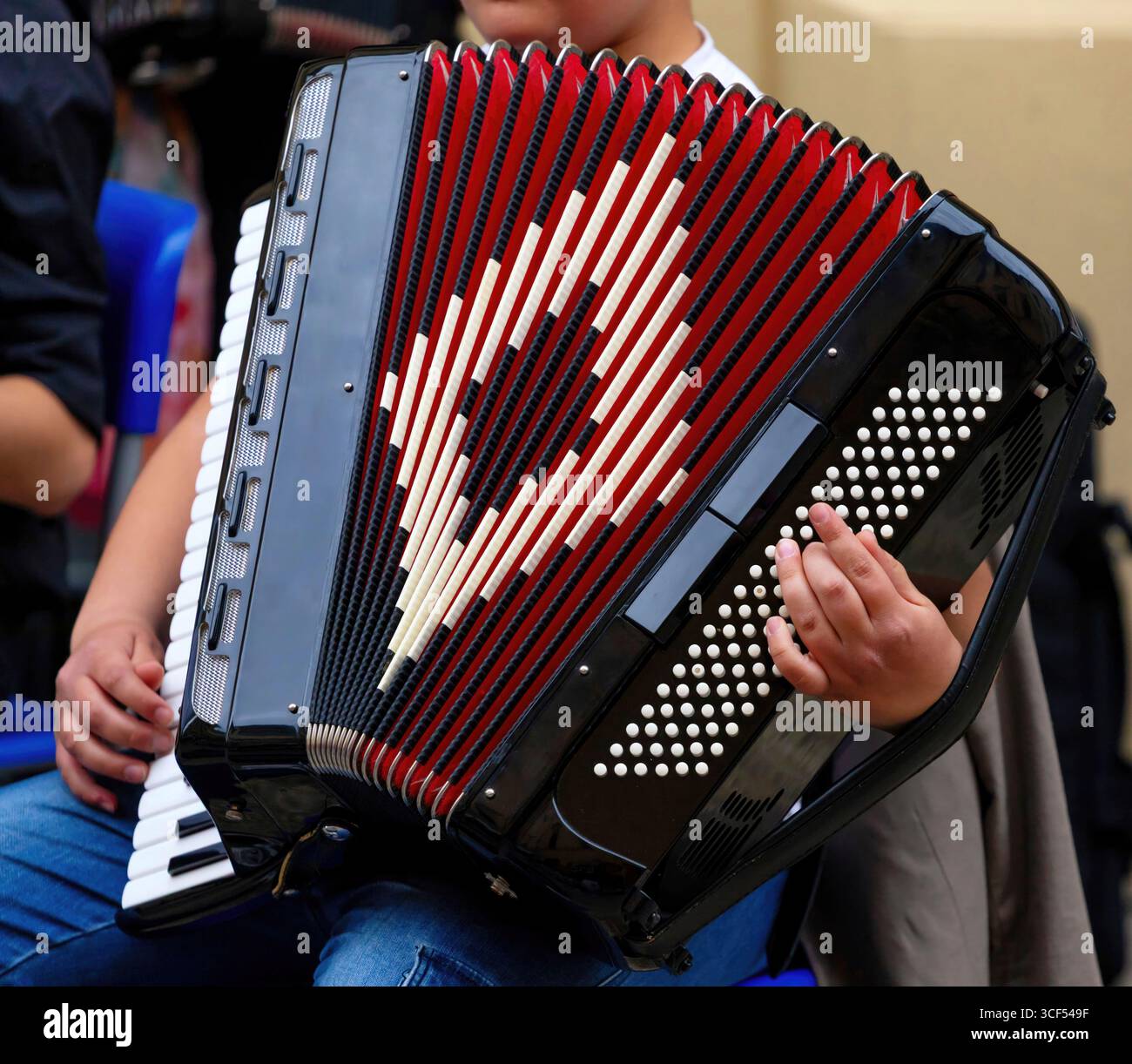 Jeune musicien jouant habilement un accordéon rouge et noir, créant une atmosphère musicale vibrante lors d'un concert de rue en plein air, captivant le public par leur talent et leur passion pour la musique Banque D'Images