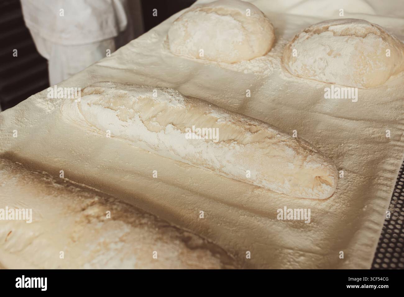 Pains crus et baguettes de pain, saupoudrés de farine, reposant sur du papier sulfurisé, attendant les mains habiles d'un boulanger dans une boulangerie animée pour leur donner vie Banque D'Images