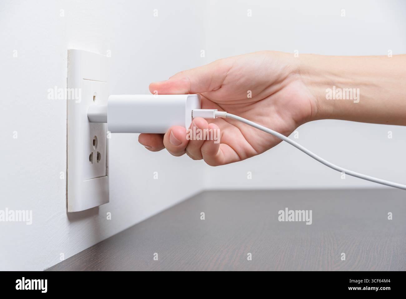 Main femelle insérant une fiche électrique blanche dans la prise Banque D'Images