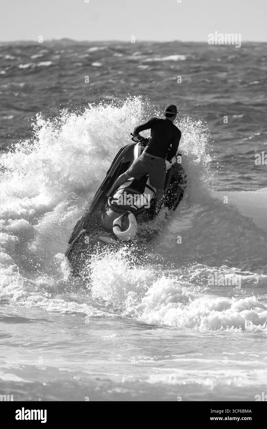Noir et blanc dramatique et intense du cavalier de jet ski Rescue perçant à travers la haute mer, naviguant puissant surf avec précision, mission solo urgente Banque D'Images