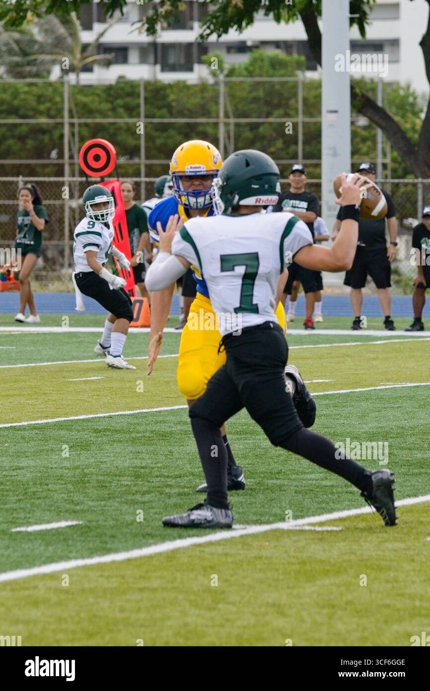 Le quarterback d'Aiea se retrouve sous la pression, quelques instants avant d'être limogé, affrontant la ruée avec calme lors d'une épreuve de football au lycée. Banque D'Images