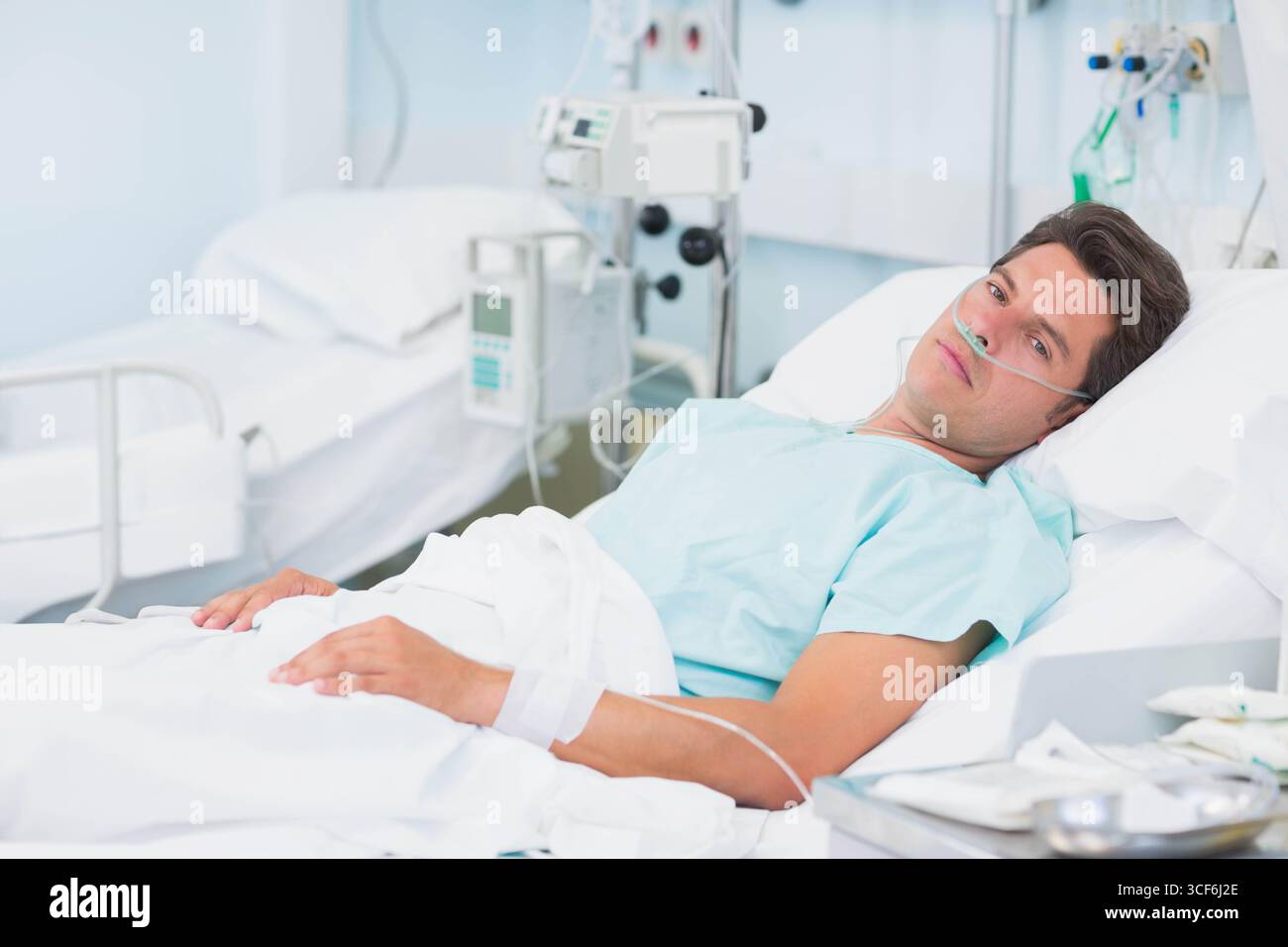 Patient hispanique de sexe masculin adulte moyen allongé sur le lit d'hôpital portant une blouse bleu clair, utilisant une canule nasale Banque D'Images