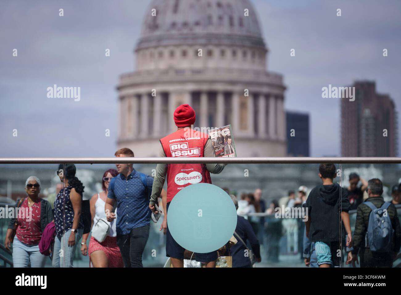 Un vendeur officiel de Big issue vend des copies au public à l'extrémité sud du Millennium Bridge où la cathédrale Saint-Paul est vue en arrière-plan, le 20 août 2025, à Londres, en Angleterre. Banque D'Images