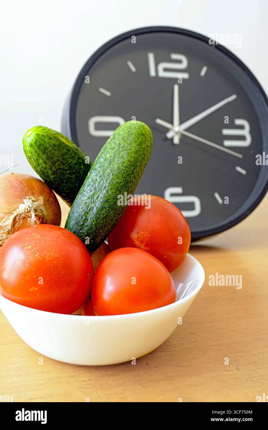Tomates, concombre et oignon près de l'horloge montrant 12 :10. Horaire de jeûne intermittent. Produits frais avec des habitudes alimentaires chronométrées. Alimentation et bien-être Banque D'Images