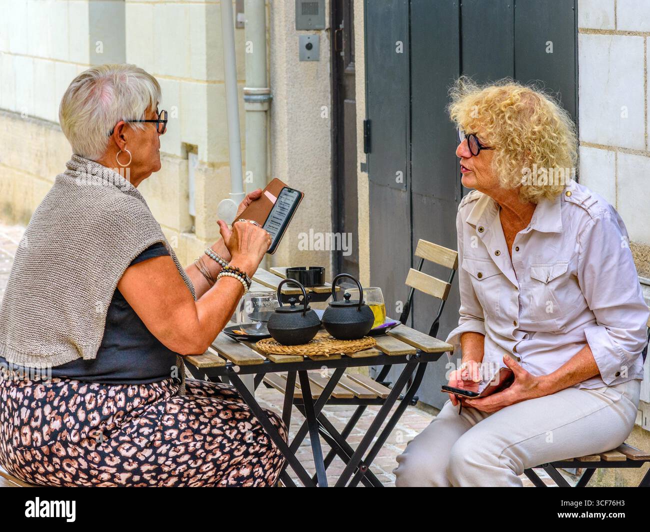 Deux femmes matures échangeant des notes sur leur smartphone tout en étant assises à la table de café en plein air dans le vieux quartier de Tours, Indre-et-Loire (37), France. Banque D'Images
