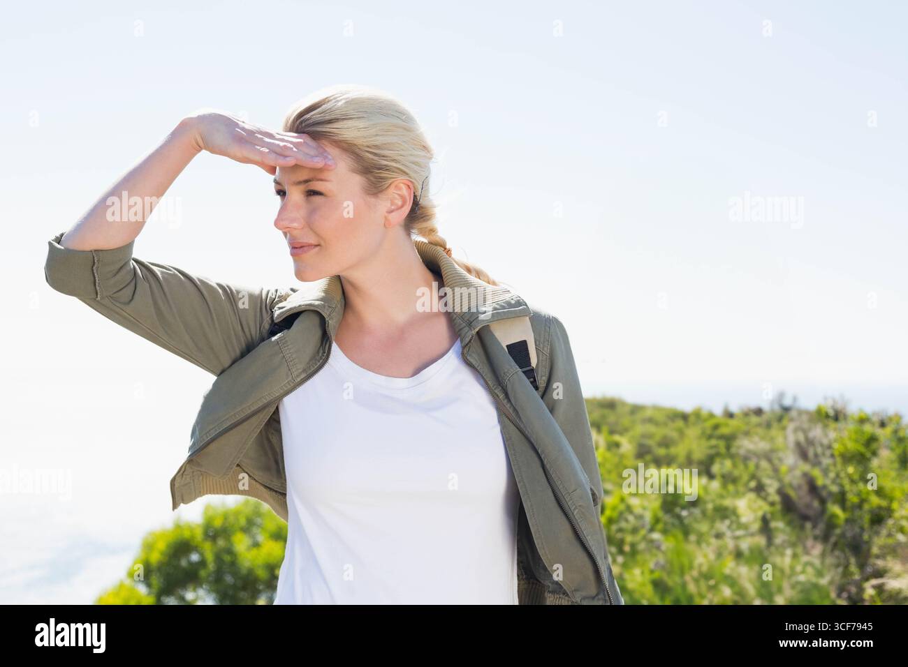 Femme randonnant les yeux d'ombrage de colline côtière et portant sac à dos tout en portant une veste vert olive Banque D'Images