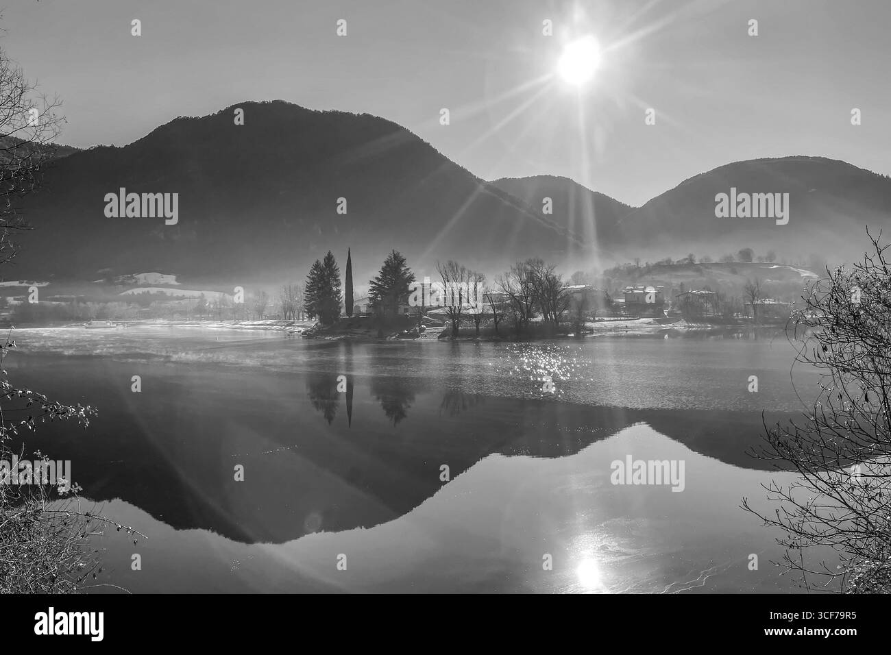 Vue d'hiver noir et blanc du lac Idro en Lombardie Italie avec le soleil lumineux des montagnes alpines et des arbres reflétés sur la scène atmosphérique de l'eau calme Banque D'Images