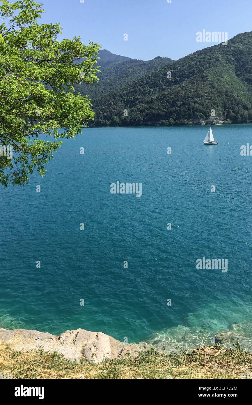 Lago di Ledro dans le Trentin Italie paysage d'été avec des montagnes vertes d'eau turquoise et un voilier blanc sur la surface calme du lac sous le ciel bleu Banque D'Images