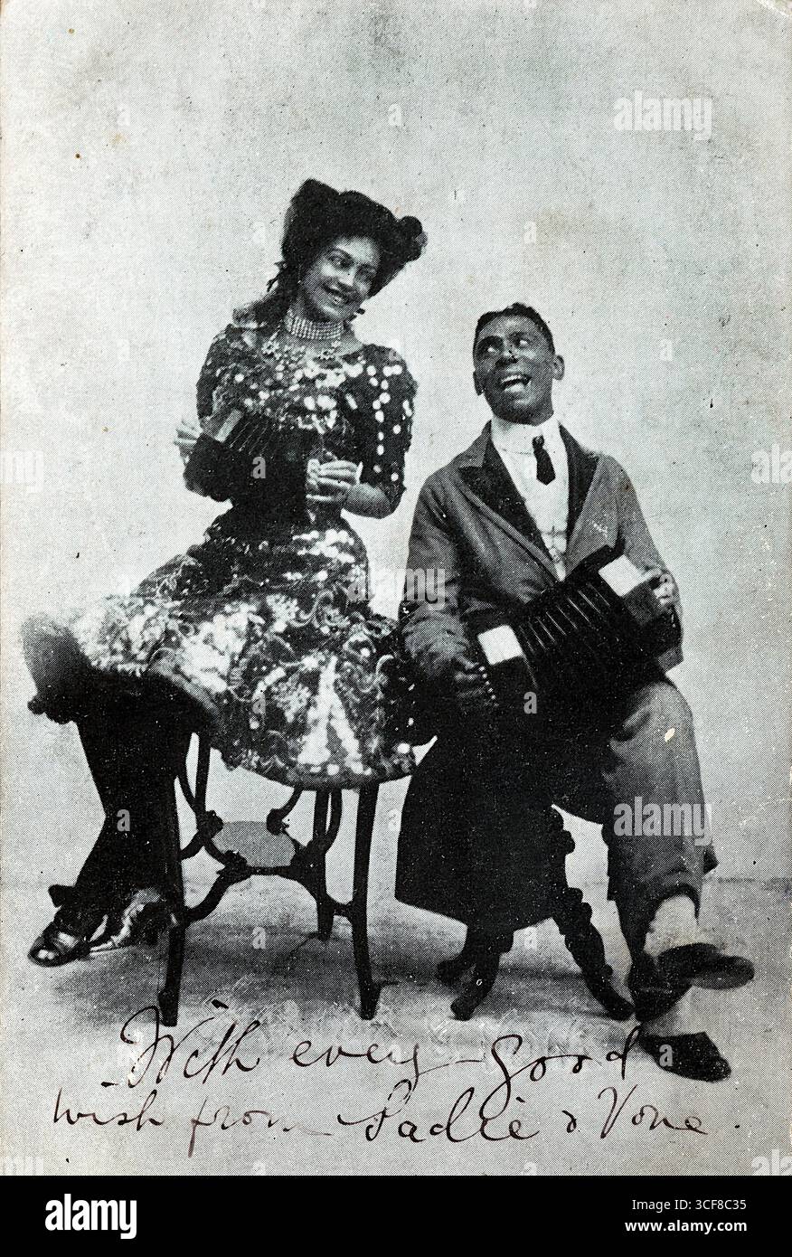 Sadie et Vone sont assis côte à côte, chacun tenant un concertina avec un calme joyeux. Leur tenue – Sadie dans une robe à motifs, Vone dans un costume et une cravate – reflète la mode du début des années 1910, tandis que leurs sourires et leur posture détendue suggèrent camaraderie et relation de scène. L’inscription manuscrite, « avec chaque bon vœu de Sadie & Vone », ajoute chaleur et flair personnel. Publiée dans le cadre de la série théâtrale de J. Richardson (Leeds), l’image capture un moment de partenariat musical et de culture édouardienne du divertissement. Banque D'Images