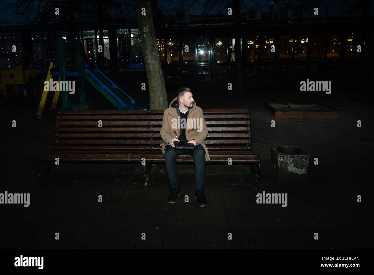Une soirée calme se déroule comme un individu seul assis sur un banc en bois, entouré par la douce lueur des lumières lointaines et un terrain de jeu paisible, évoquant moi Banque D'Images