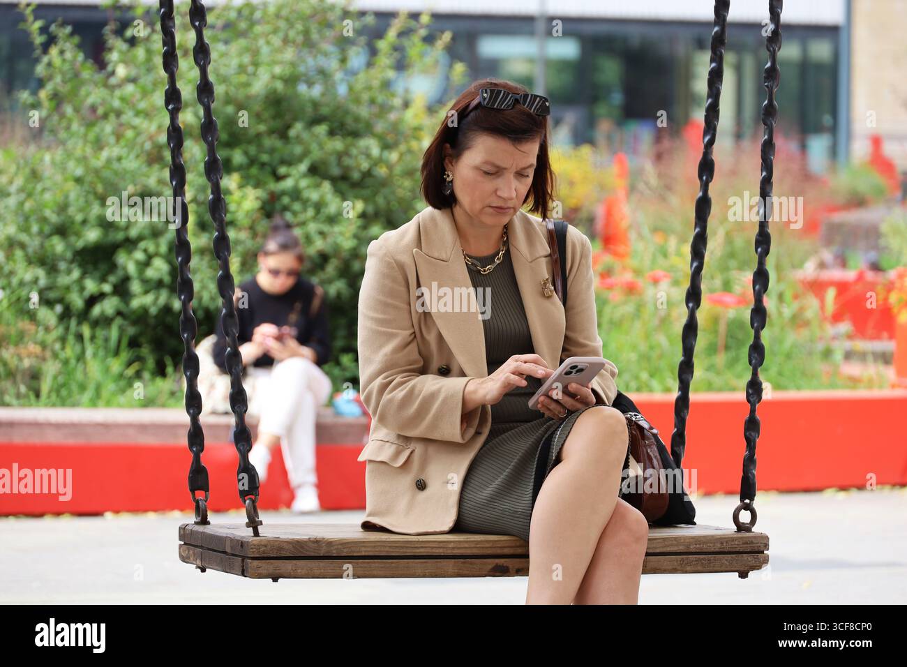 Femme utilisant un smartphone assis sur une balançoire dans la rue de la ville en été Banque D'Images