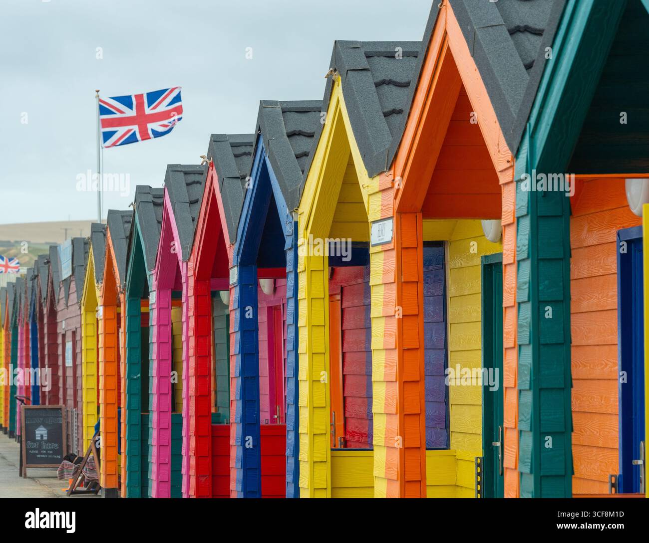 Des cabanes de plage traditionnelles peintes de couleurs vives bordent la promenade, avec un drapeau de l'Union Jack flottant, dans la station balnéaire de Saltburn, dans le North Yorkshire, au Royaume-Uni. Banque D'Images