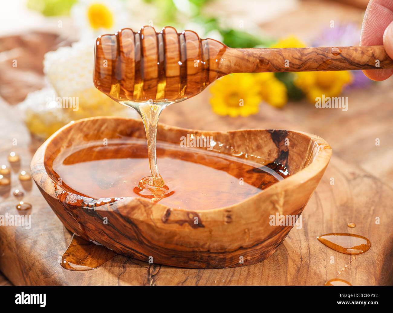 Miel goutte à goutte de la cuillère en bois dans un bol en bois avec du miel, fleurs de printemps sont sur la table en bois près. Banque D'Images