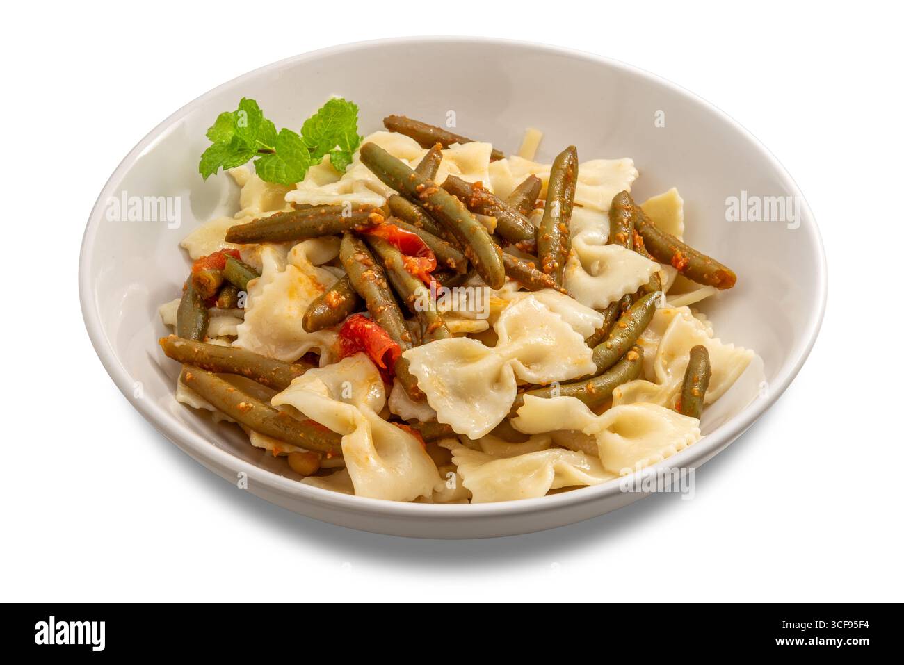 Pâtes noeud papillon avec haricots verts et sauce tomate, garnies d'un brin de menthe, sur une assiette blanche isolée sur blanc avec chemin de coupe inclus Banque D'Images