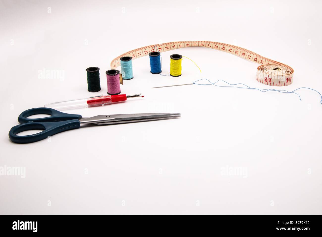 Les essentiels de couture sur fond blanc : bobines de coton coloré, ciseaux, aiguille filetée, ruban à mesurer et cueilleur de points, parfait pour l'artisanat, tailo Banque D'Images