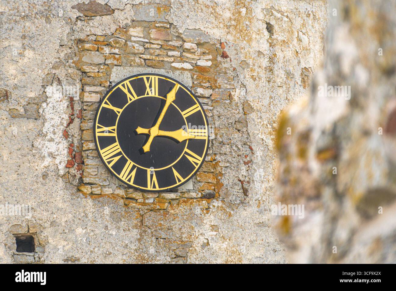Horloge vintage avec des chiffres romains dorés sur fond noir, sur une surface de brique et de pierre altérée, symbolisant l'histoire et l'architecture intemporelle Banque D'Images