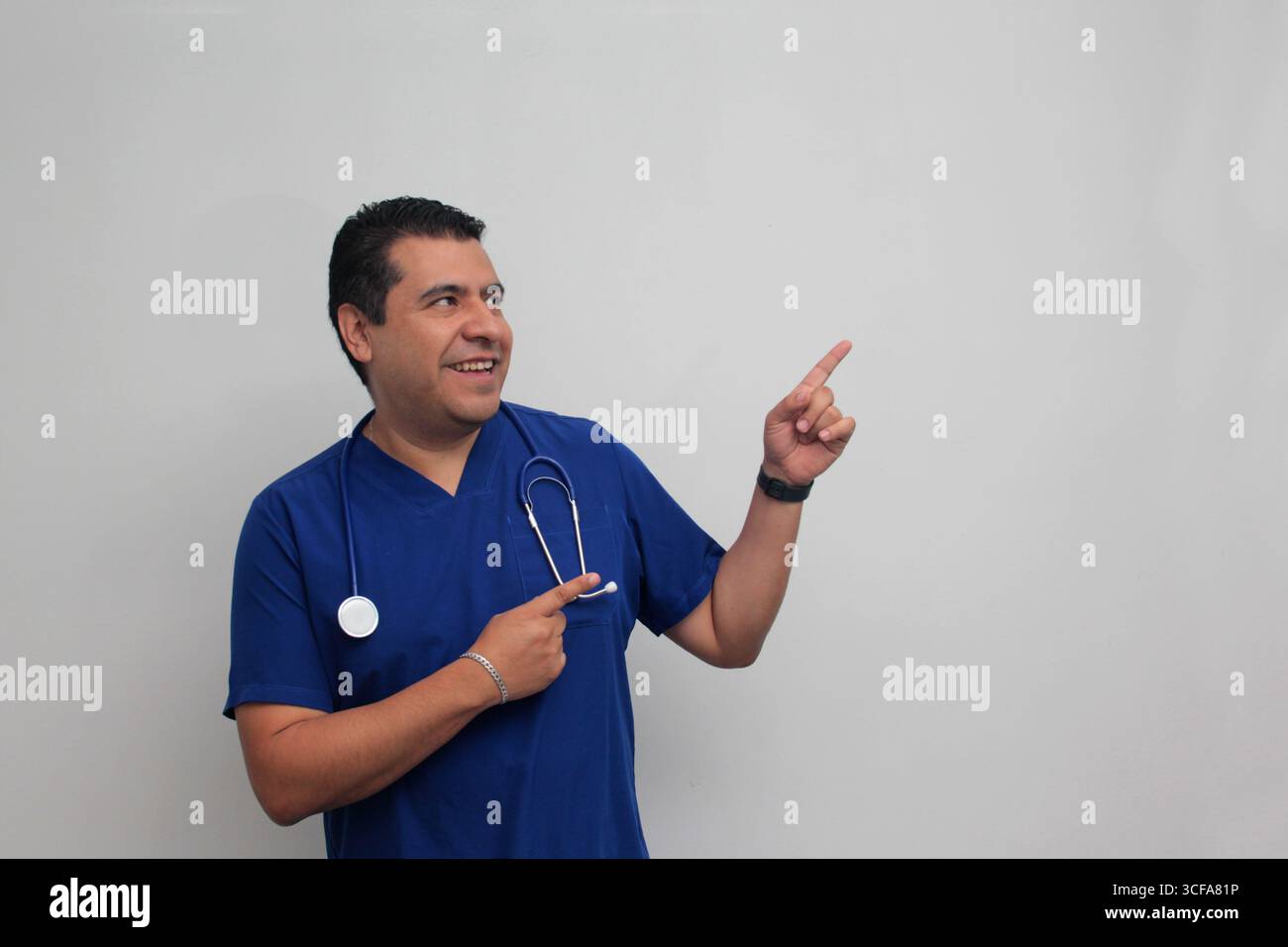 Médecin spécialiste latino-américain à la peau foncée avec un stéthoscope pointe avec son doigt avec une expression de joie et de surprise Banque D'Images Médecin spécialiste latino-américain à la peau foncée avec un stéthoscope pointe avec son doigt avec une expression de joie et de surprise Banque D'Images