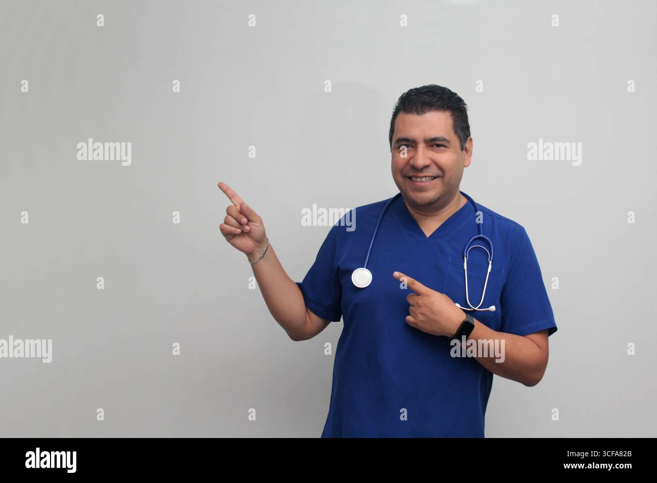 Médecin spécialiste latino-américain à la peau foncée avec un stéthoscope pointe avec son doigt avec une expression de joie et de surprise Banque D'Images Médecin spécialiste latino-américain à la peau foncée avec un stéthoscope pointe avec son doigt avec une expression de joie et de surprise Banque D'Images