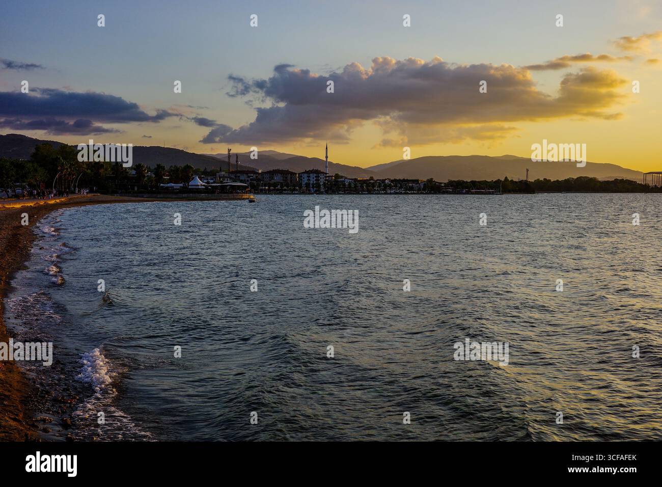 Coucher de soleil coloré sur Başiskele Sahil avec plage de sable, vagues calmes et paysage urbain contre les montagnes à Kocaeli, Turquie. Banque D'Images