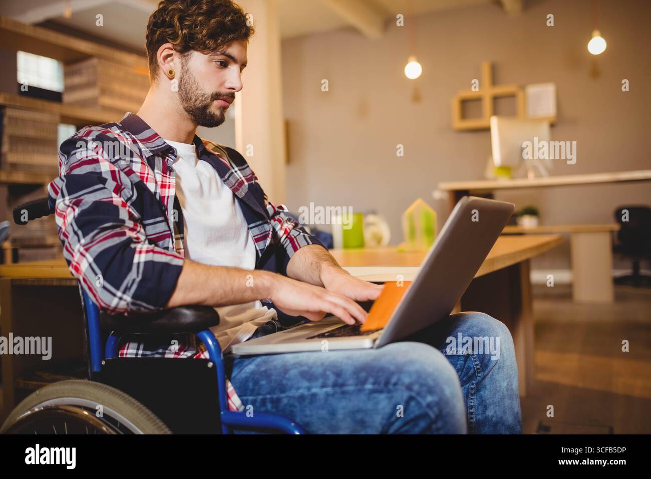 Ordinateur portable reposant sur un fauteuil roulant à côté de bureaux en bois sous des lampes suspendues suspendues dans le bureau de co-working Banque D'Images