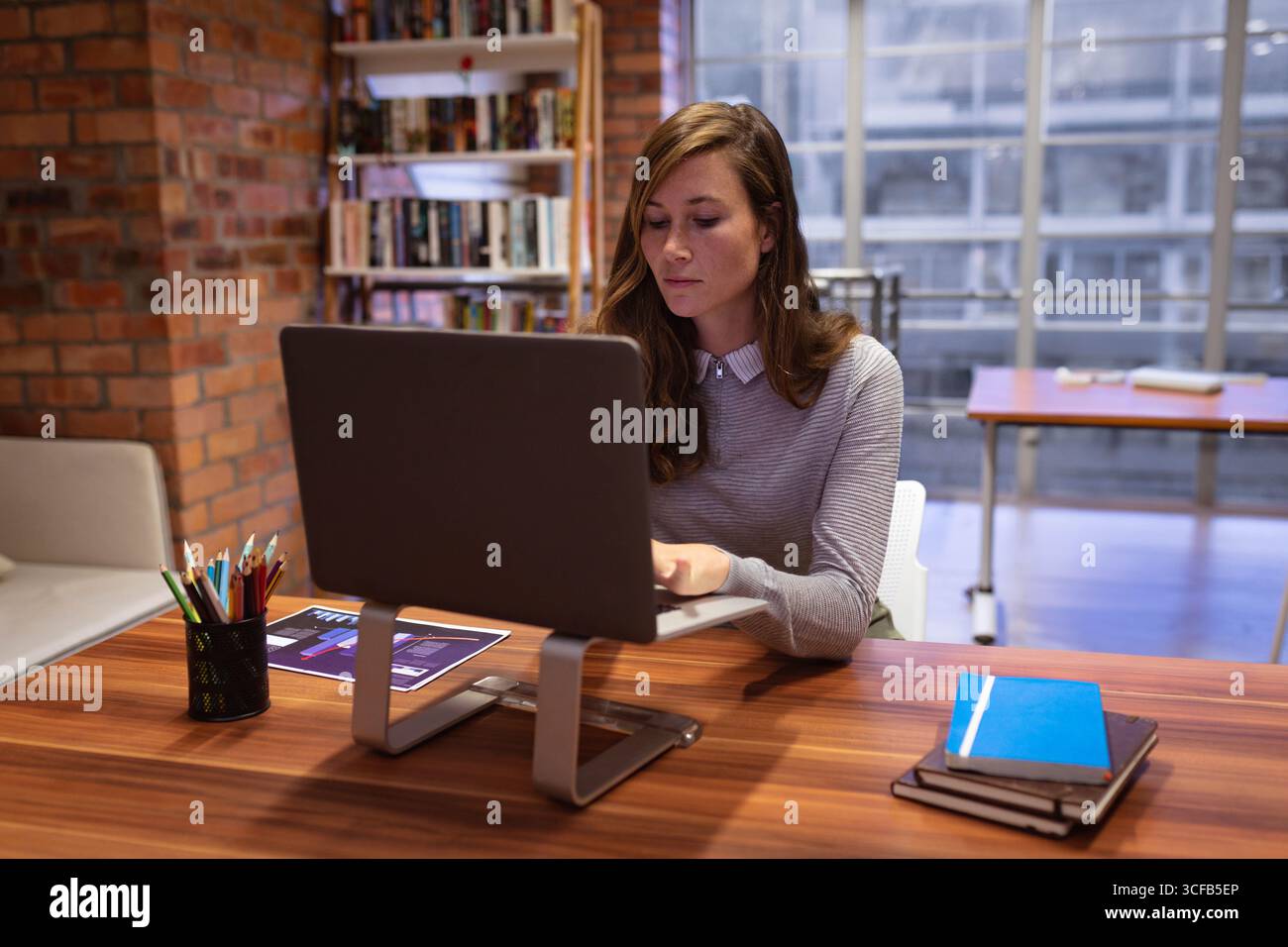 Ordinateur de bureau assis sur un bureau en bois avec un graphique imprimé à crayon et des cahiers près de la fenêtre Banque D'Images