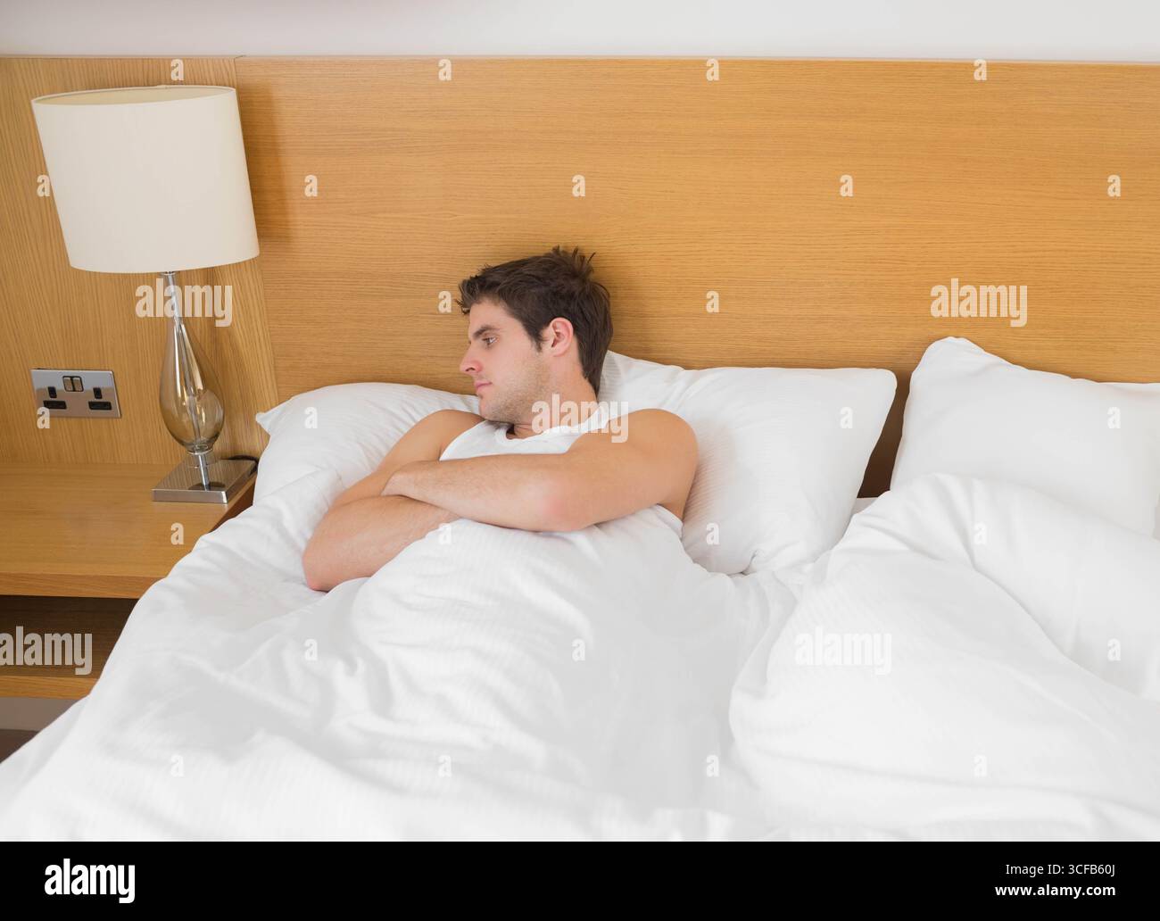 Homme portant un débardeur inclinable sur le lit à côté de la tête de lit et lampe de chevet dans la chambre Banque D'Images
