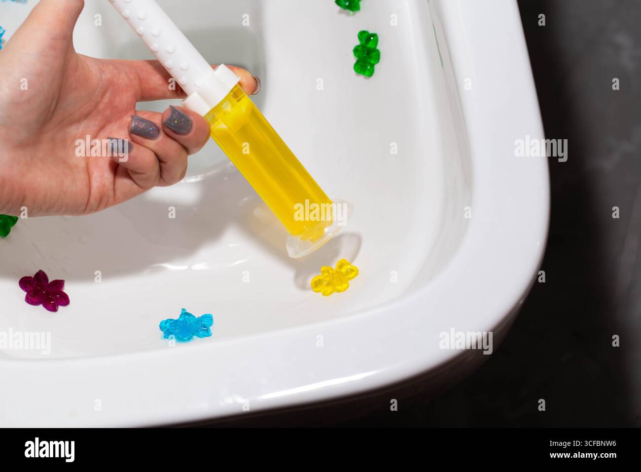 Gel jaune dans une seringue dans une main sur le fond d'une toilette. Nettoyage et désinfection des toilettes, effet antibactérien Banque D'Images