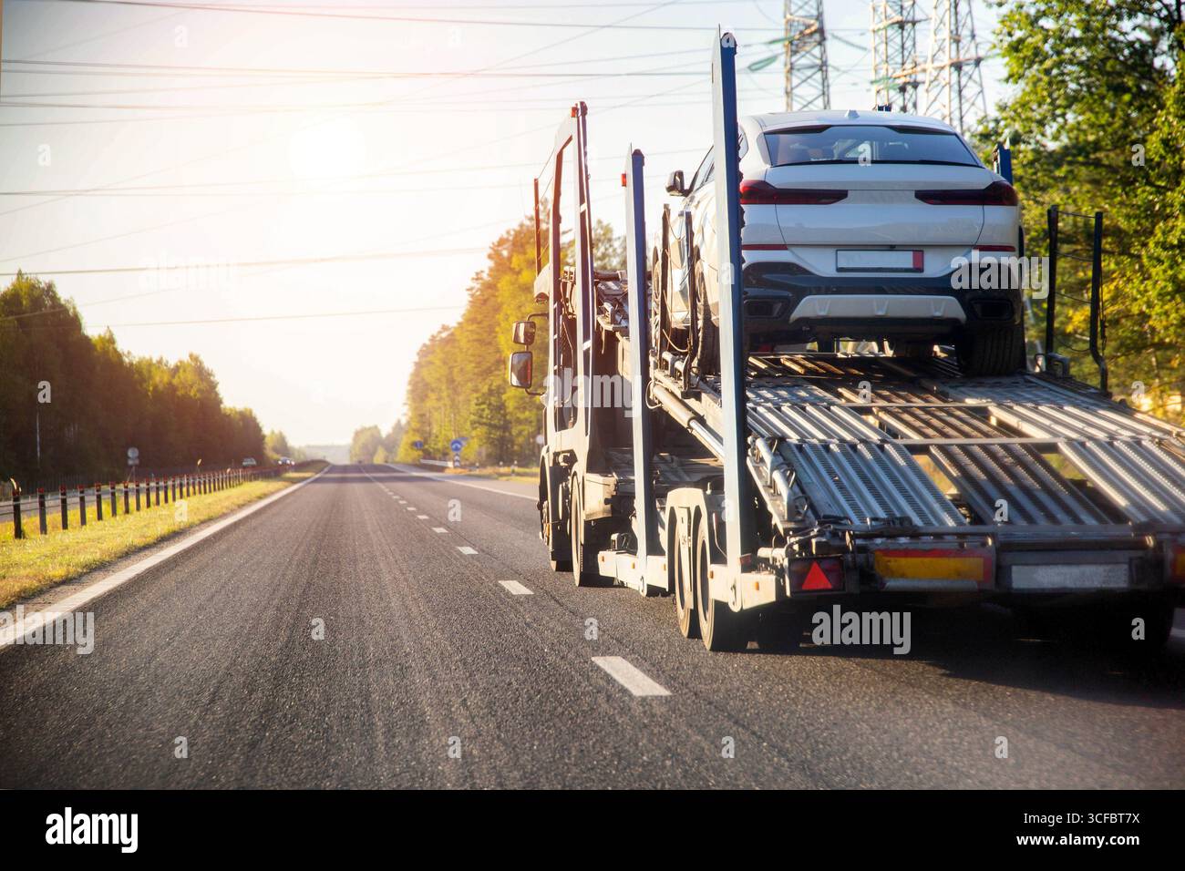 Un camion avec un camion de remorquage de semi-remorque transporte une voiture de tourisme en panne à un centre de service de voiture le long de la route en été dans le contexte de Banque D'Images