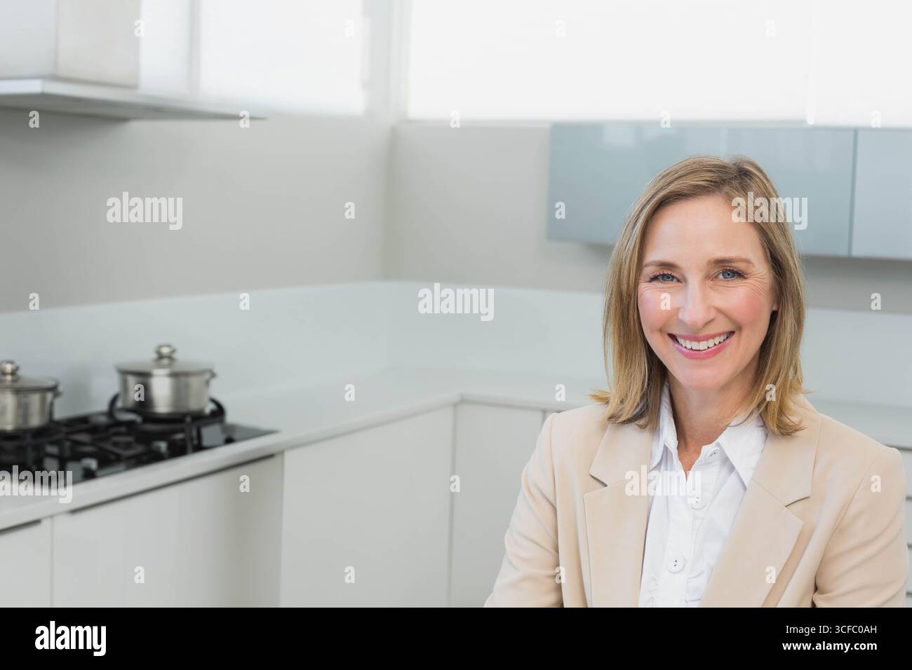 Femme souriant tout en se tenant debout dans la cuisine à la maison par table de cuisson à gaz et pots en acier inoxydable, espace de copie Banque D'Images