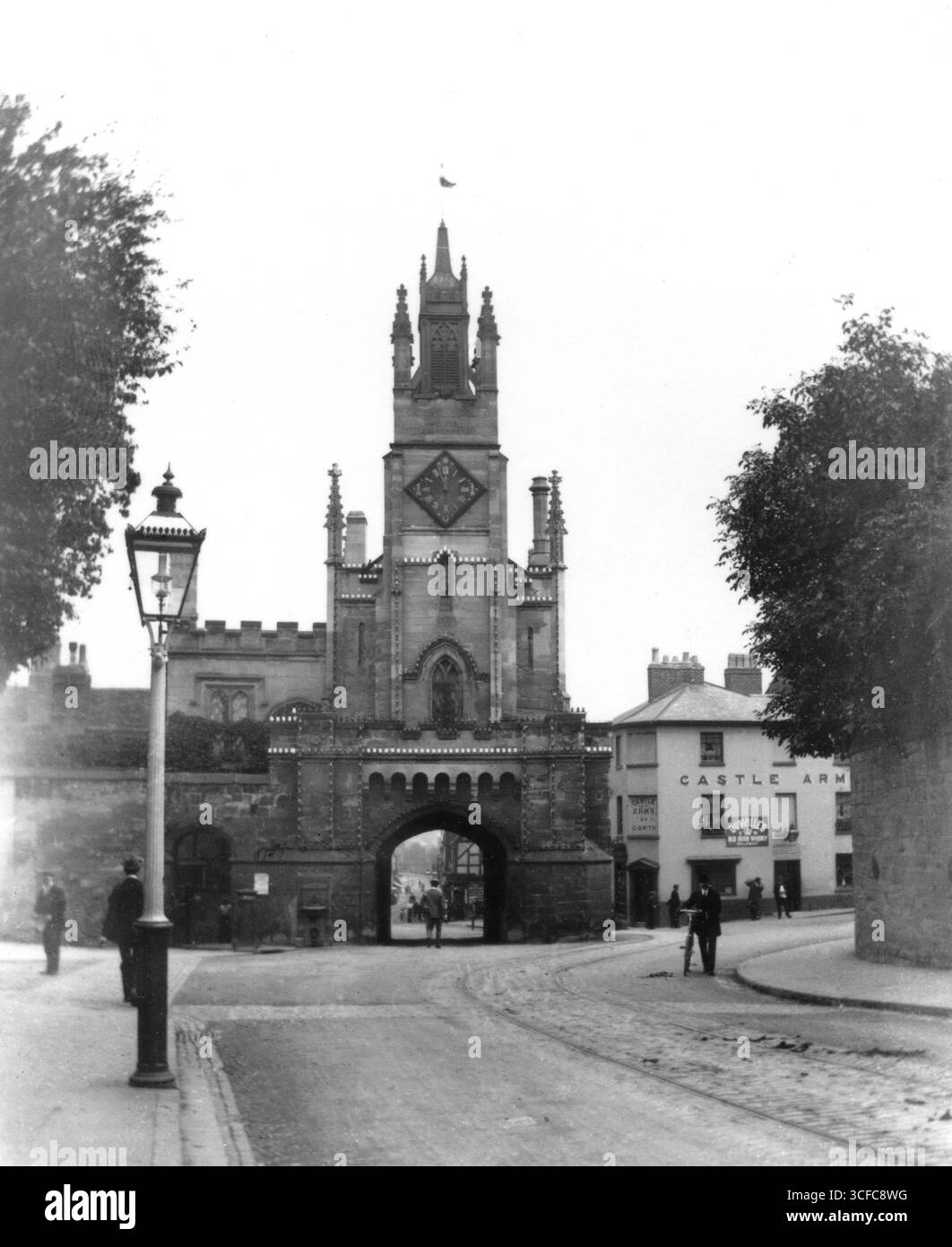 Warwickshire, Angleterre. Circa.1905 - photographie édouardienne de East Gate, une porte du XIVe siècle surmontée d'une chapelle du XVe siècle, située dans la ville de Warwick. La photographie a été prise à la jonction de jury Street et Castle Street. Adjacent à la maison de garde est la maison publique Castle Arms. Sur le mur du pub est exposée une enseigne annonçant Dunville’s Old Irish Whisky. Au premier plan, un lampadaire à gaz. Banque D'Images