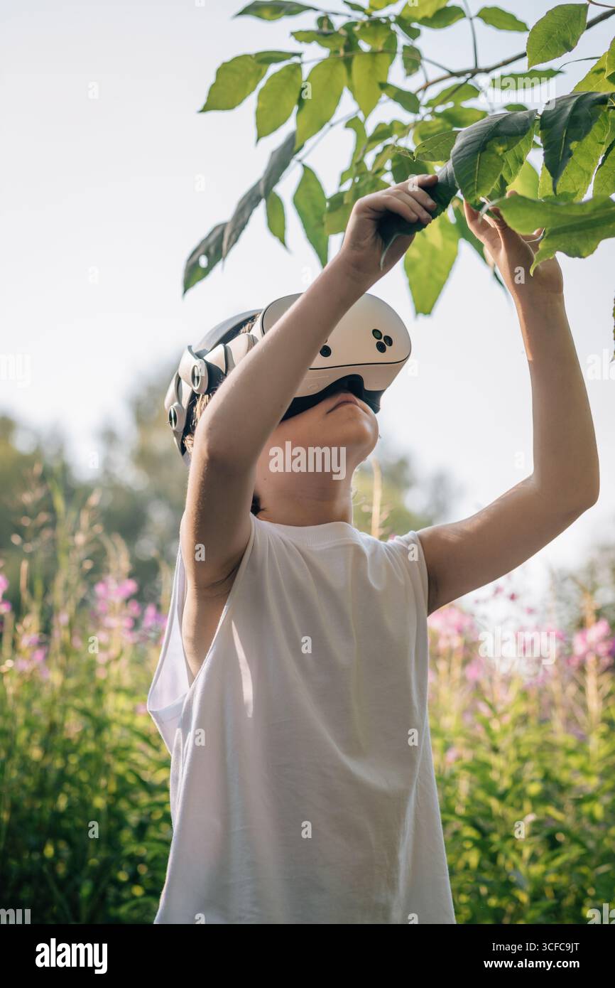 Homme enfant dans des lunettes de réalité virtuelle touche des feuilles Banque D'Images