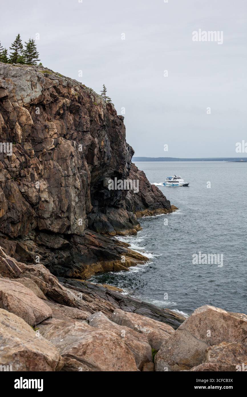 Un bateau proposant des visites du phare apparaît derrière un cli escarpé Banque D'Images