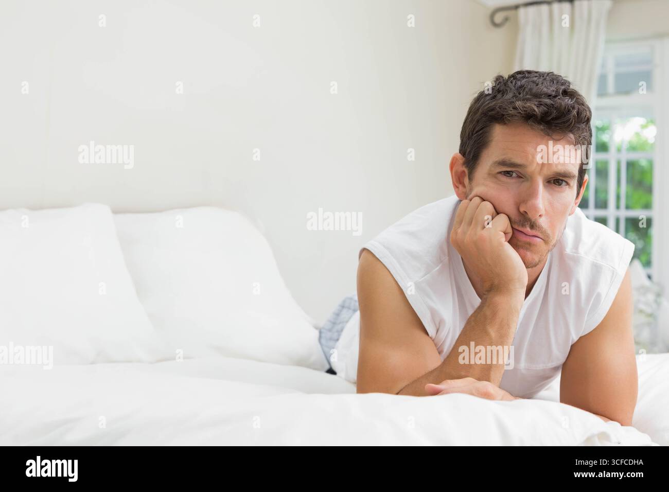Homme allongé sur le lit soutenant la tête et regardant tranquillement vers les rideaux et la fenêtre, copier l'espace Banque D'Images