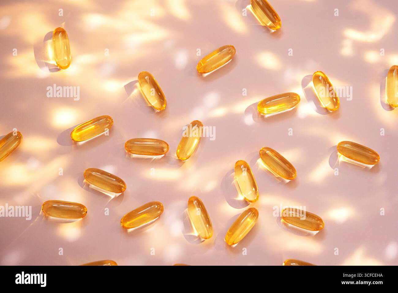 Capsules d'huile de poisson jaunes sur fond rose clair avec éblouissement du soleil et ombres. Supplément de santé pour le bien-être et l'apport nutritionnel. Banque D'Images