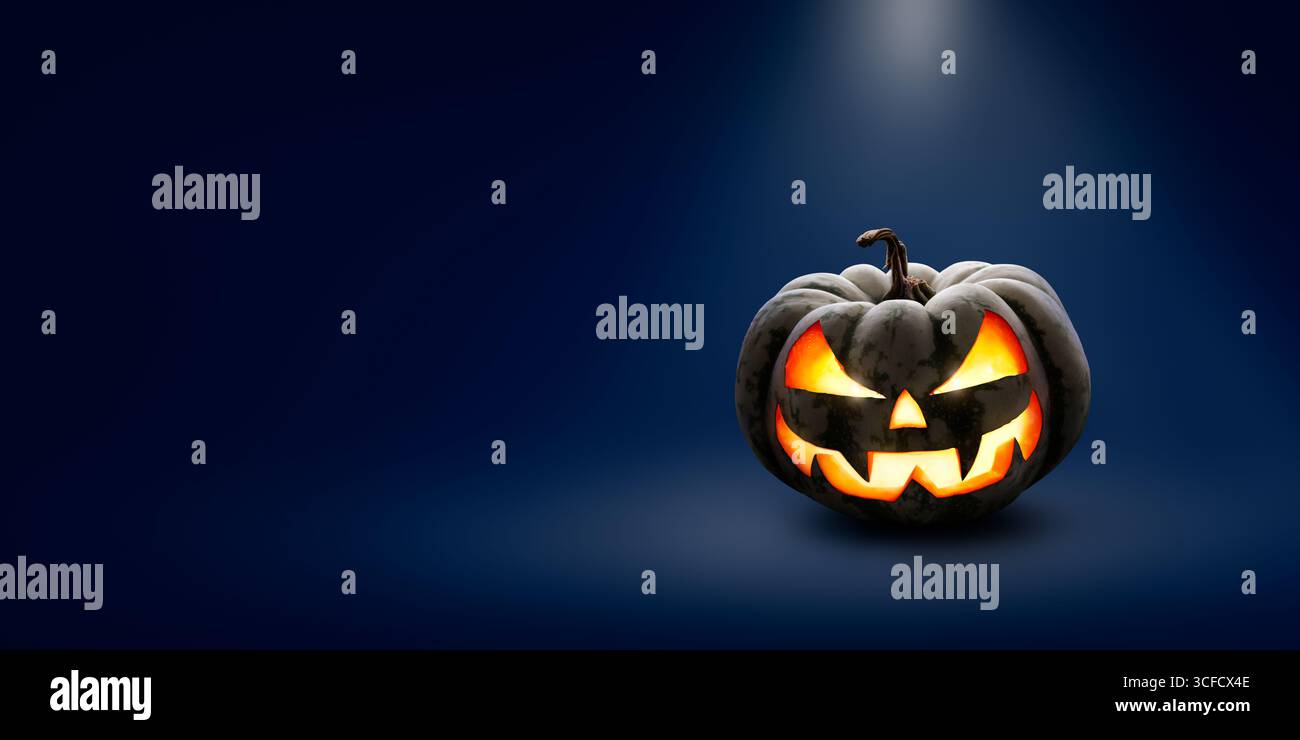 Un halloween effrayant éclairé Jack O Lantern la nuit sous la lueur d'un projecteur sur un large fond bleu foncé avec espace de copie. Banque D'Images Un halloween effrayant éclairé Jack O Lantern la nuit sous la lueur d'un projecteur sur un large fond bleu foncé avec espace de copie. Banque D'Images