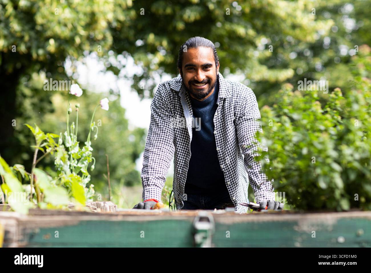 Un homme souriant tend vers un jardin luxuriant, habillé de façon décontractée avec un feuillage vert autour de lui. Allemagne Banque D'Images