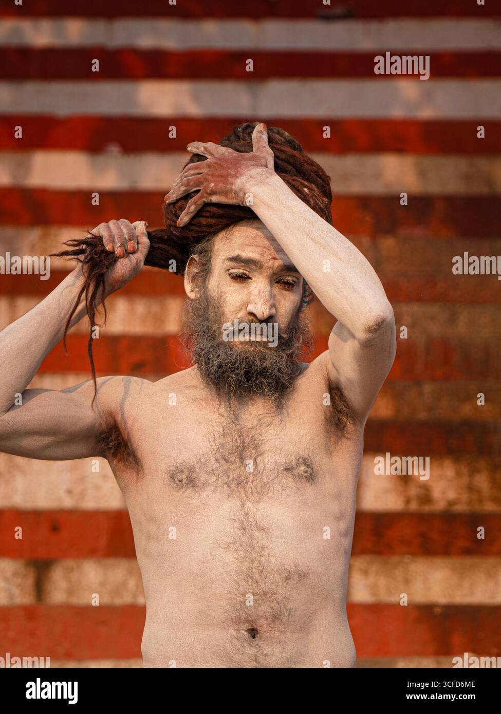 Naga Sadhu (ascète hindou) couvert de frêne sacré (Bhasma) arrangeant ses dreadlocks sur les Ghats de Varanasi. Banque D'Images
