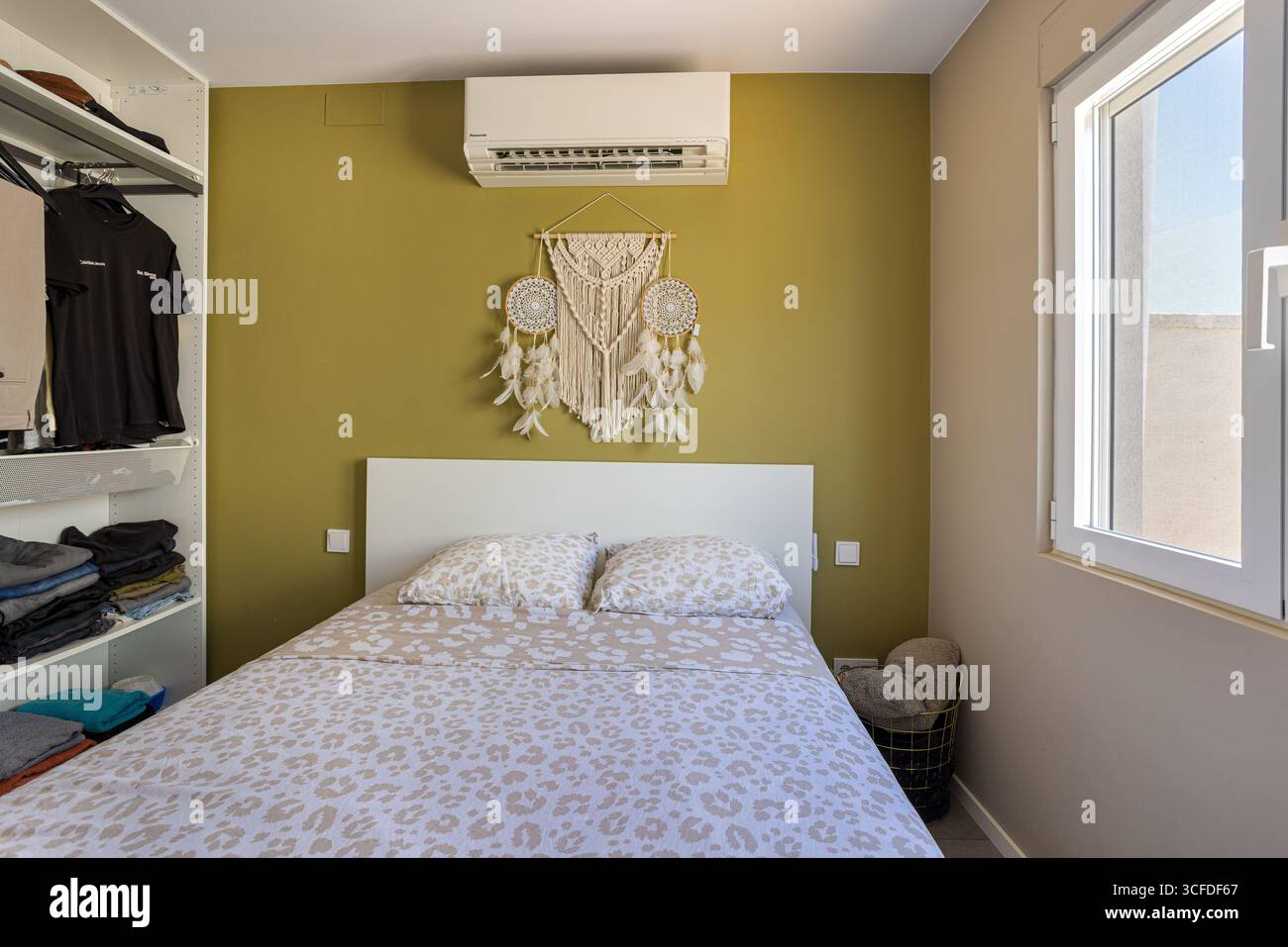 Chambre avec mur décoratif vert, lit double avec literie à motifs et étagères ouvertes. Banque D'Images