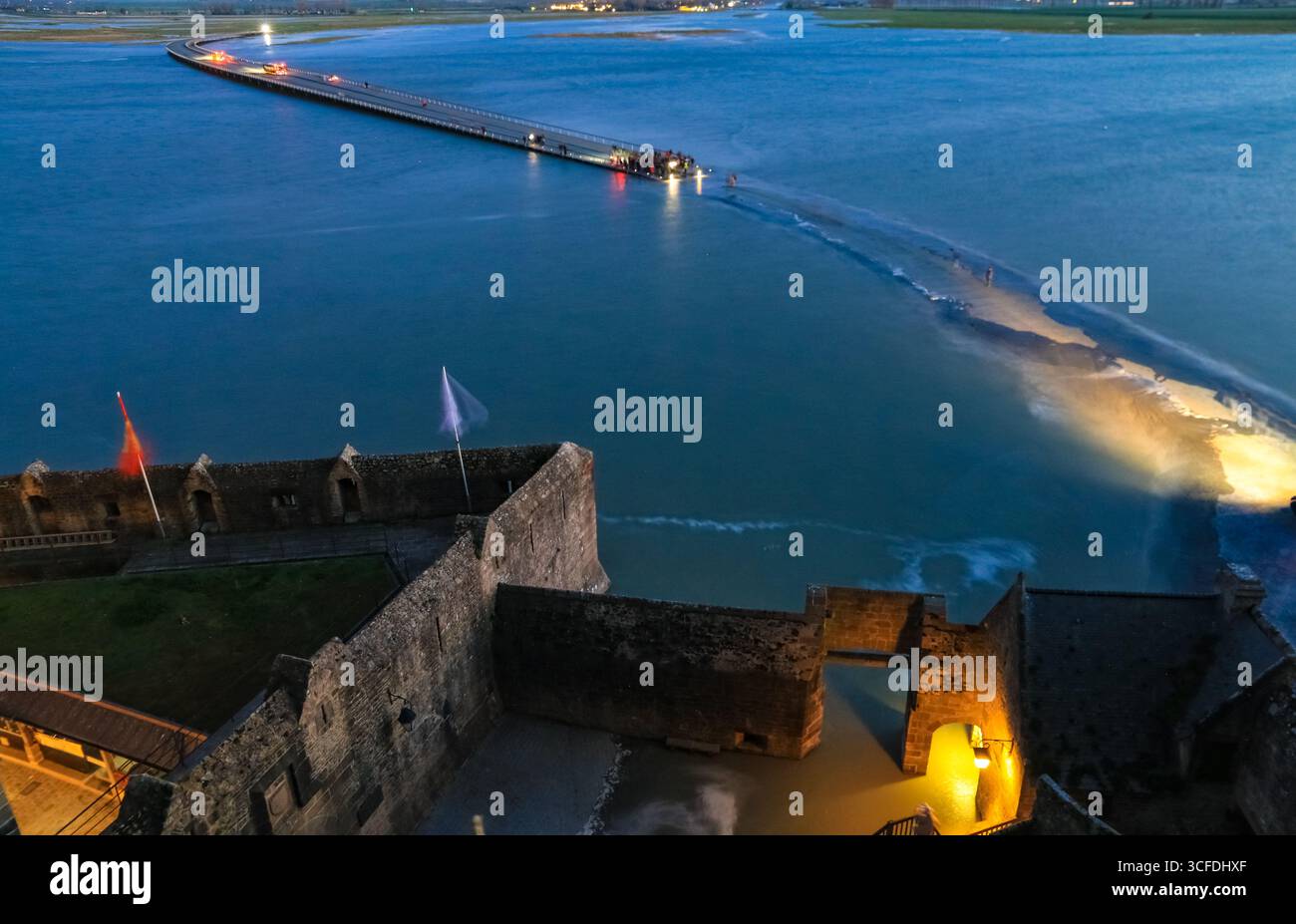 Depuis une terrasse sur l’île, une vue imprenable s’ouvre sur l’entrée fortifiée du Mont‑Saint‑Michel et son pont de liaison, comme en fin de soirée... Banque D'Images