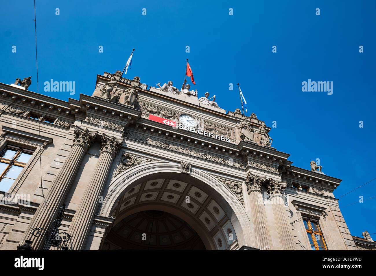 Zurich, Suisse, 19 août 2025. Façade d'entrée du bâtiment de la gare centrale de Zurich HB. Regardant vers le haut shot, jour d'été ensoleillé, grande horloge et drapeau, pas de poo Banque D'Images