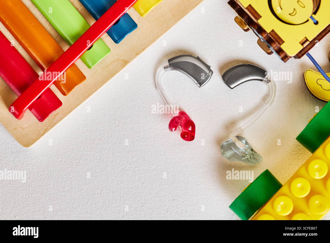 Audiologie pour enfants, aides auditives fraîches reposent sur une surface entourée de jouets colorés, symbolisant l'apprentissage ludique et la découverte pour les enfants, à plat Banque D'Images